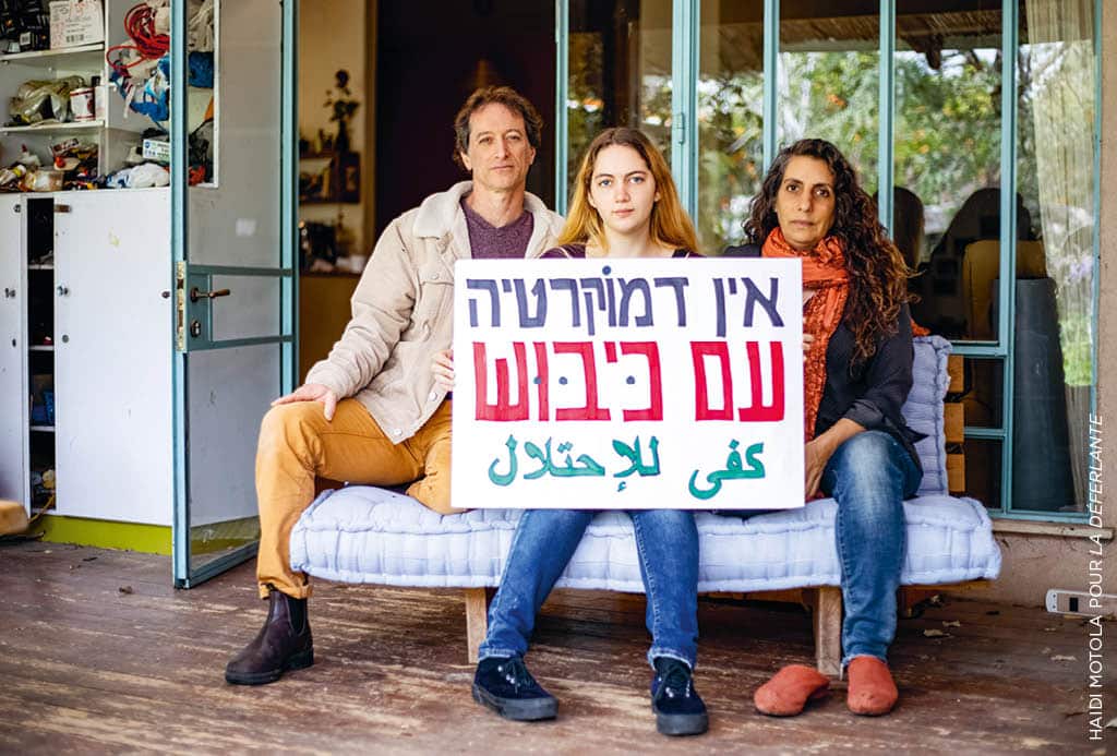 Sofia Orr et ses parents, chez eux, à Pardes Hanna. Sofia s’apprête à refuser en août 2023 de faire le service militaire. Elle a la chance – le « privilège », dit-elle – de bénéficier du soutien de ses parents. Sur la pancarte, en hébreu : « Il n’y a pas de démocratie sous occupation », et en arabe (ligne du dessous) : « Assez avec l’occupation ». Photo : Haidi Motola pour La Déferlante